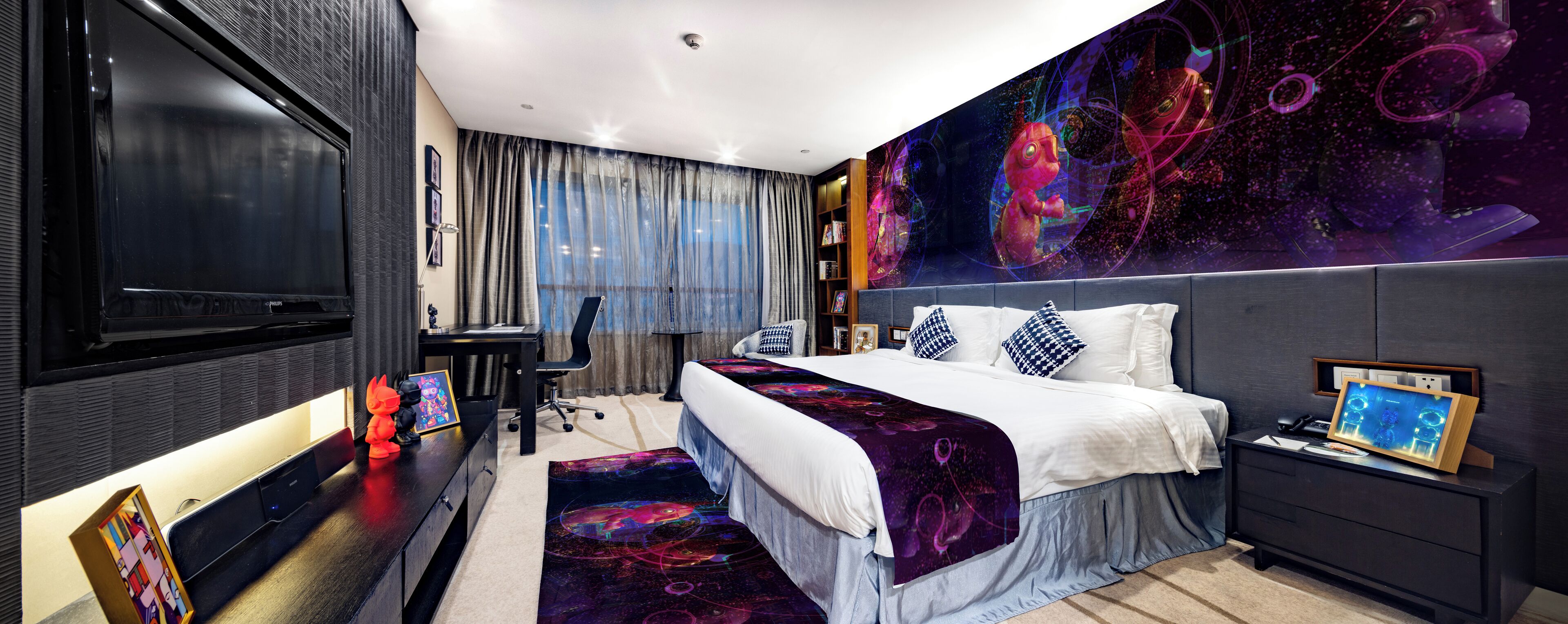 A modern hotel room with a large bed, a desk, a TV, and a wall mural.
