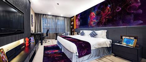 A modern hotel room with a large bed, a desk, a TV, and a wall mural.