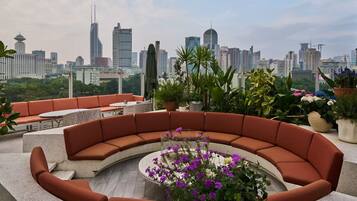 A rooftop terrace with a curved seating area, potted plants, and a city skyline view.