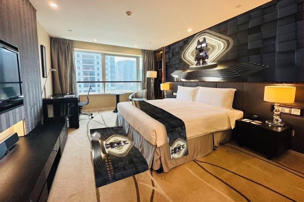 Ein modernes Hotelzimmer mit einem großen Bett, einem Schreibtisch, einem Fernseher und Blick auf die Stadt.
