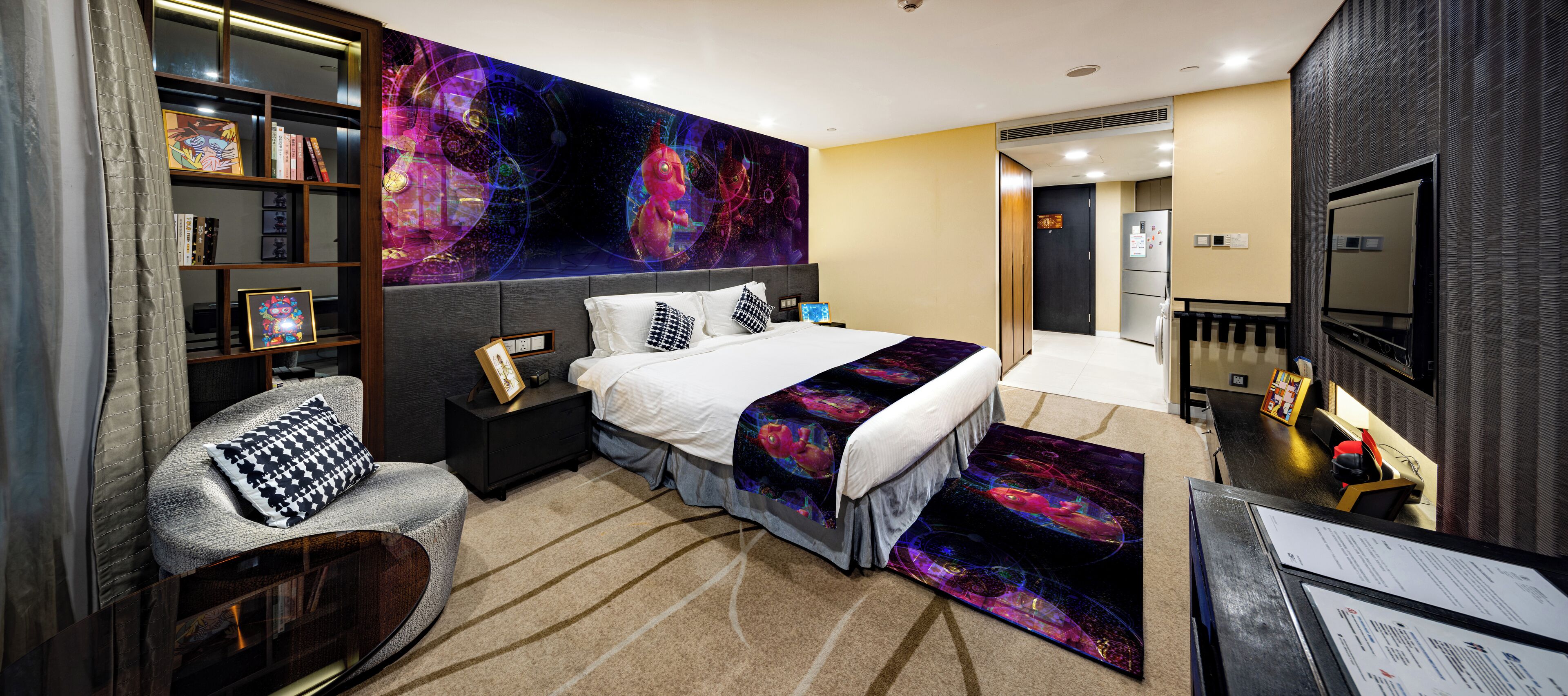 Une chambre d’hôtel moderne dotée d’un grand lit, d’un coin salon avec un canapé et un fauteuil, d’une bibliothèque et d’un grand tableau abstrait accroché au mur.