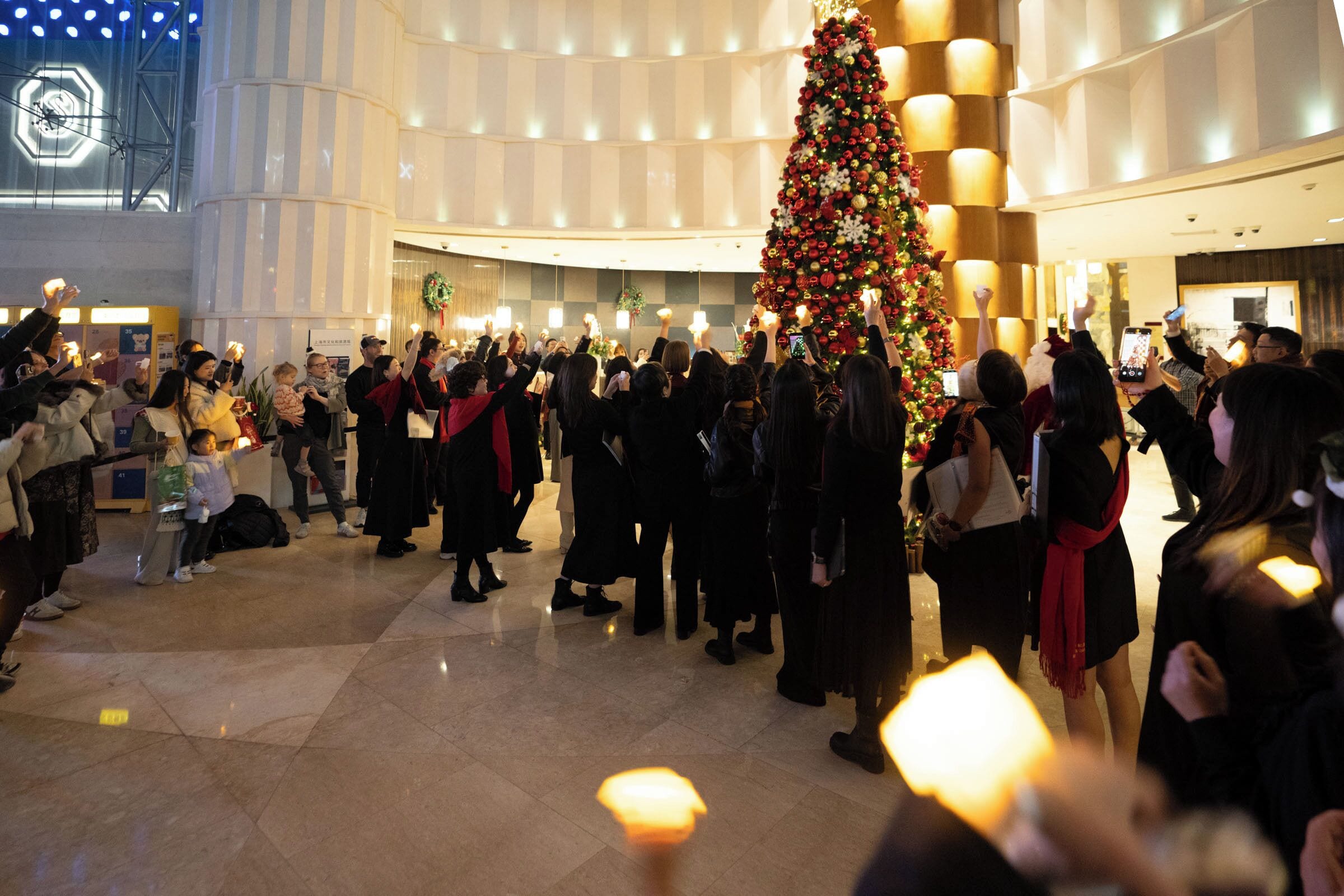 A large indoor space with a prominent Christmas tree, a checkered floor, and a high ceiling with recessed lighting.