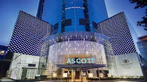 Un edificio moderno con un evidente cartello "ASCOTT", caratterizzato da un ingresso circolare e strutture in vetro circostanti con motivi illuminati.