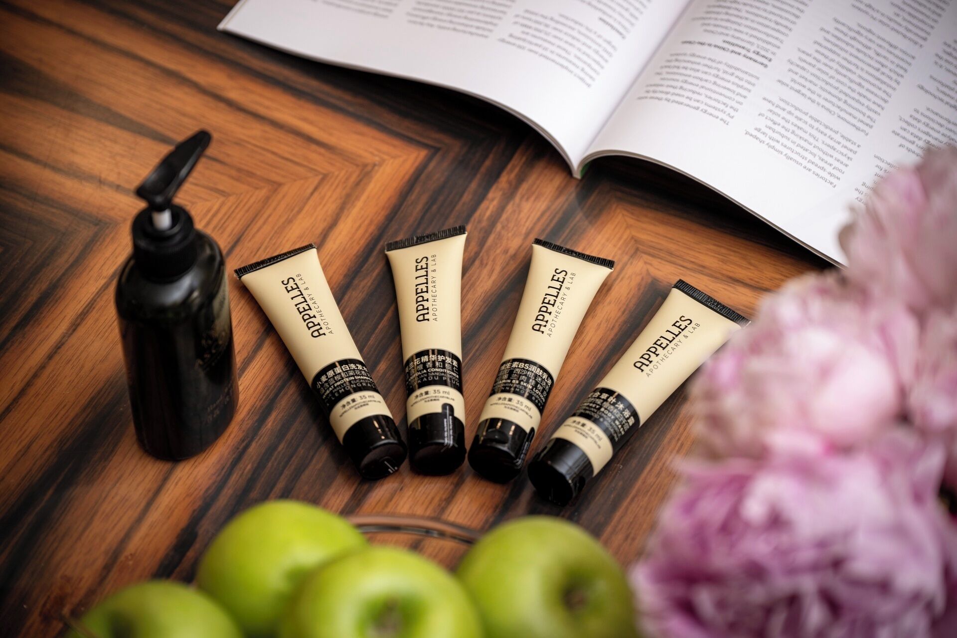A wooden surface with four tubes of APPELLES, a black bottle, and a book.