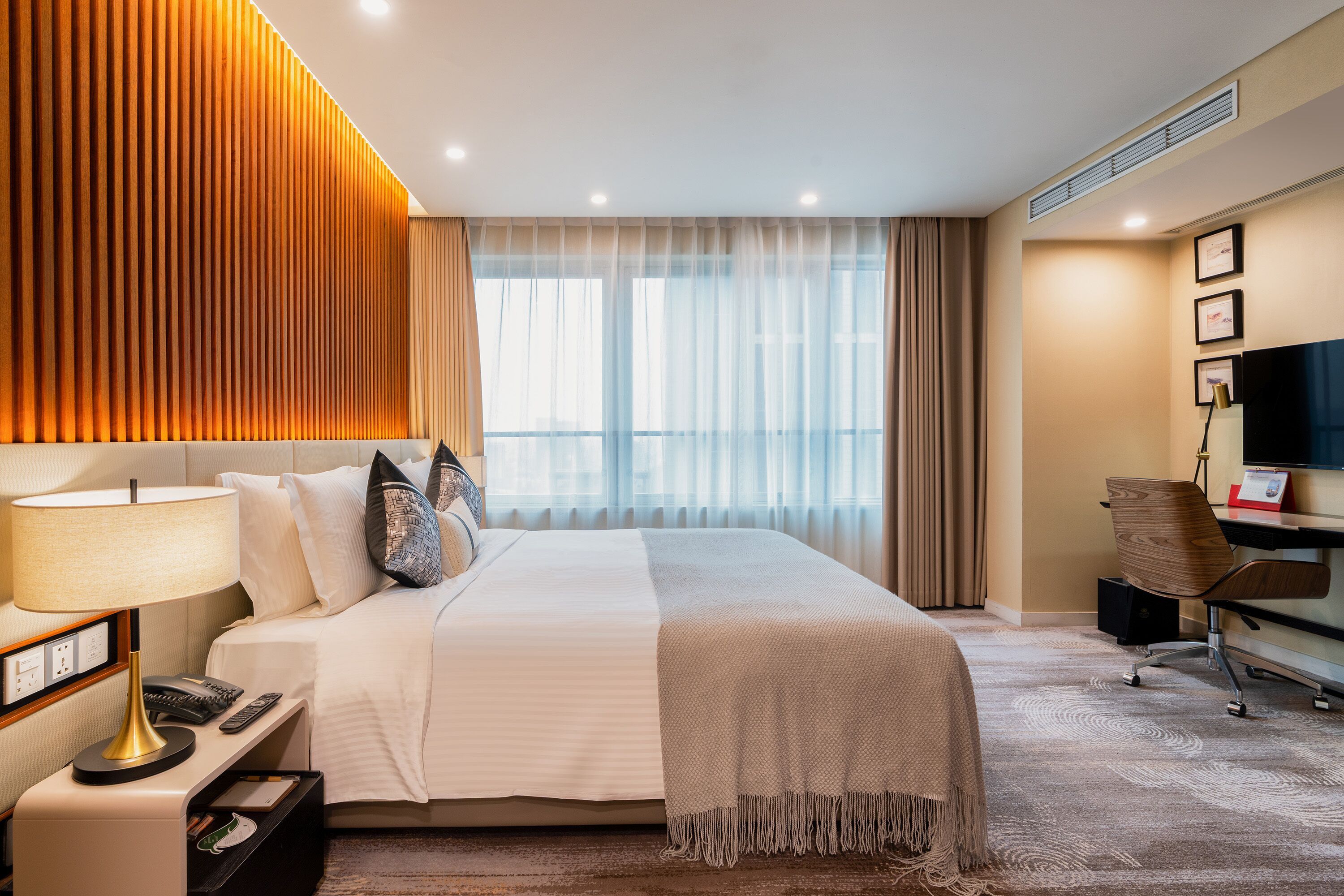 Ein Hotelzimmer mit Bett, Nachttisch, Lampe und Schreibtisch mit Stuhl.
