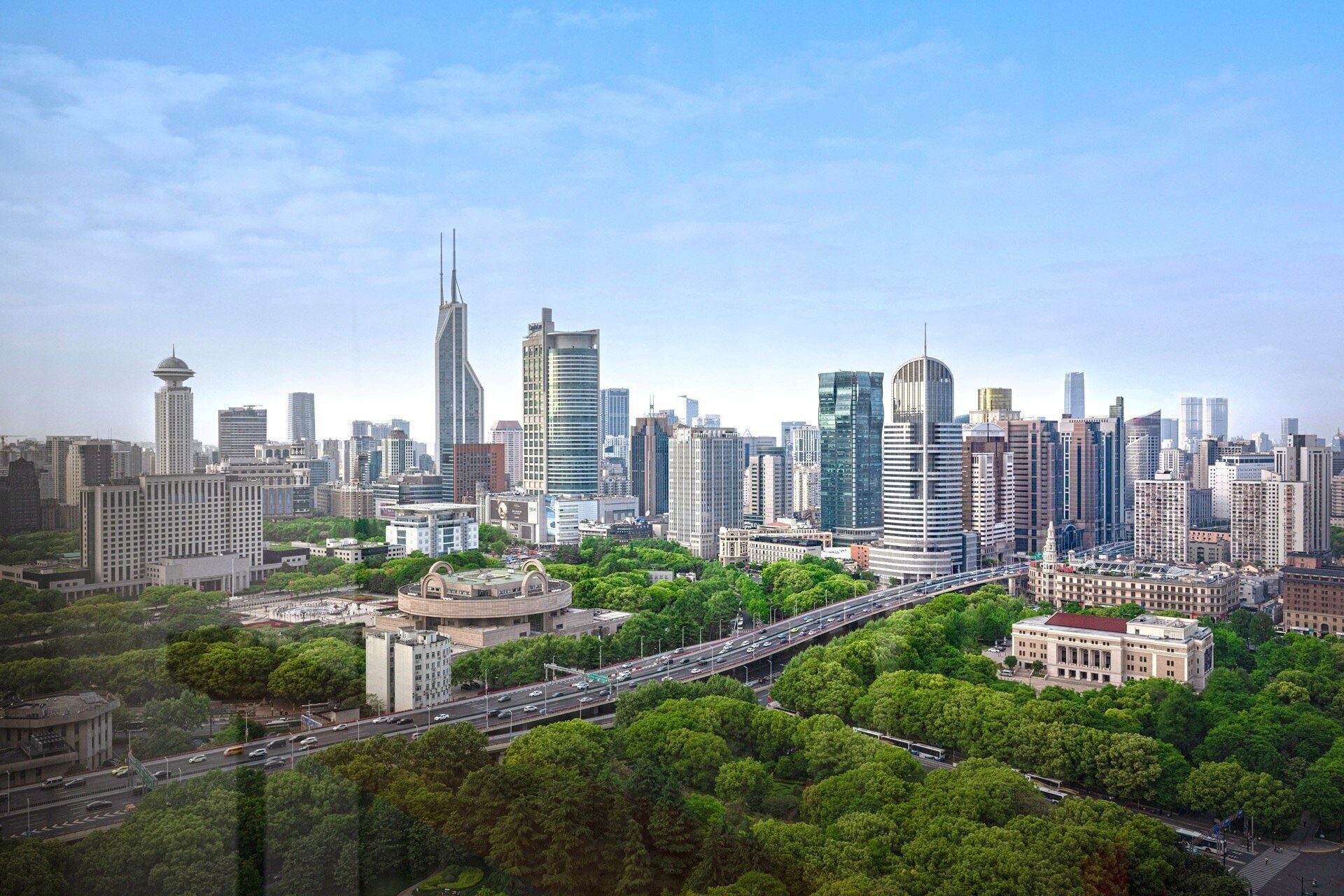Un paysage urbain avec des immeubles modernes de grande hauteur, une autoroute et des espaces verts environnants.