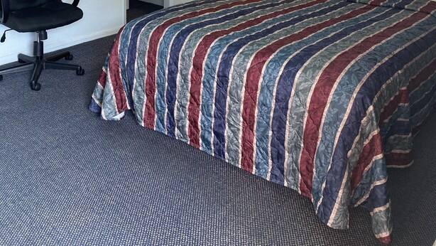 Una habitación de hotel con cama, escritorio, silla, mesita de noche y lámpara de pared.