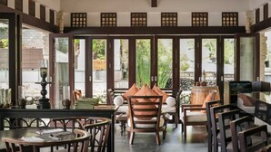 Un vaste espace intérieur aménagé avec des meubles en bois, de grandes fenêtres et un plafond recouvert de chaume.