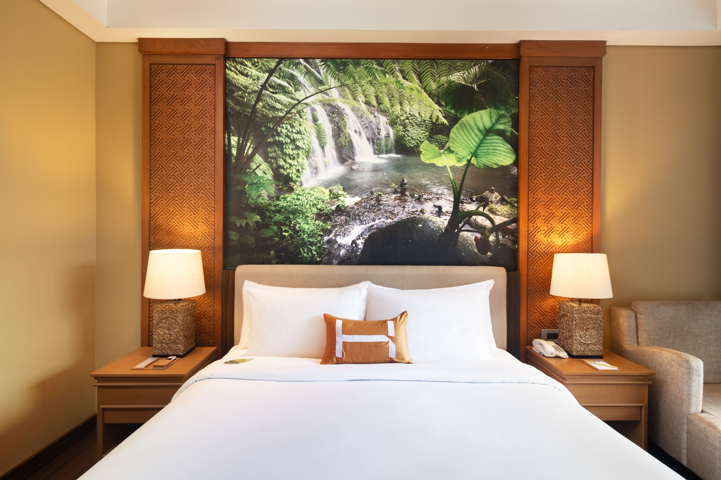 A hotel room with a large bed, two bedside tables with lamps, a chair, and a wall with a nature-themed mural.