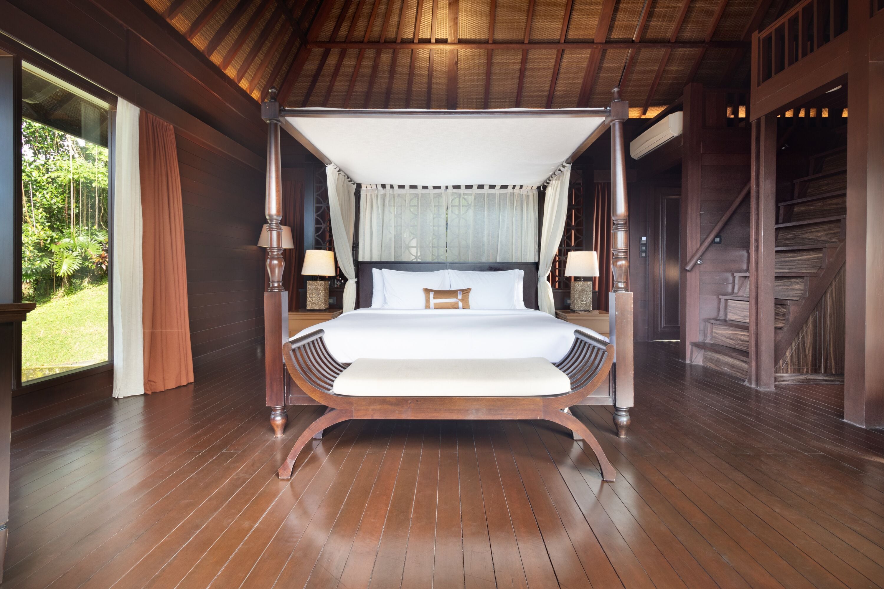 Una cama con dosel y columnas, suelo de madera y vistas al exterior.