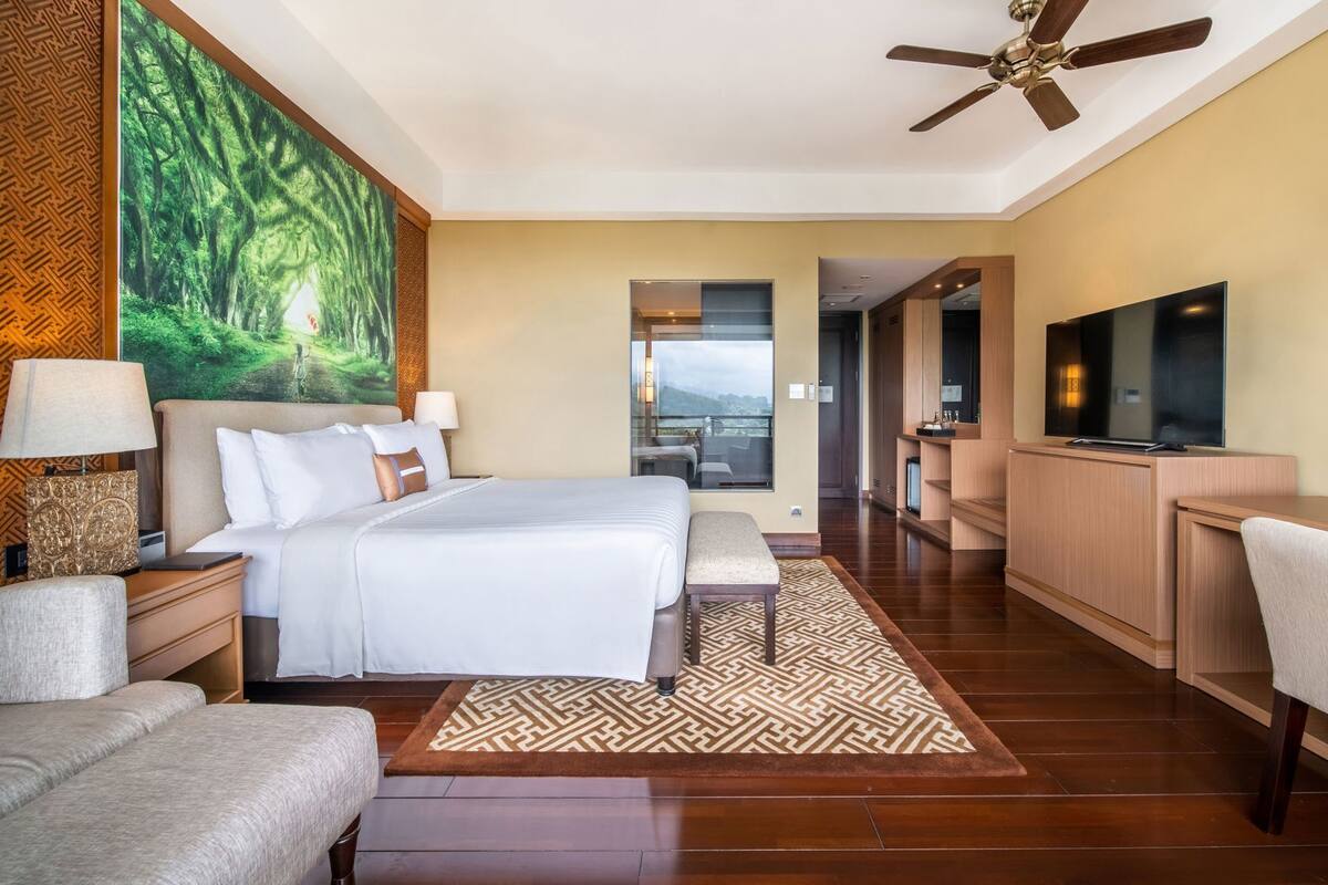 A hotel room with a bed, a TV, a desk, and a balcony with a view.