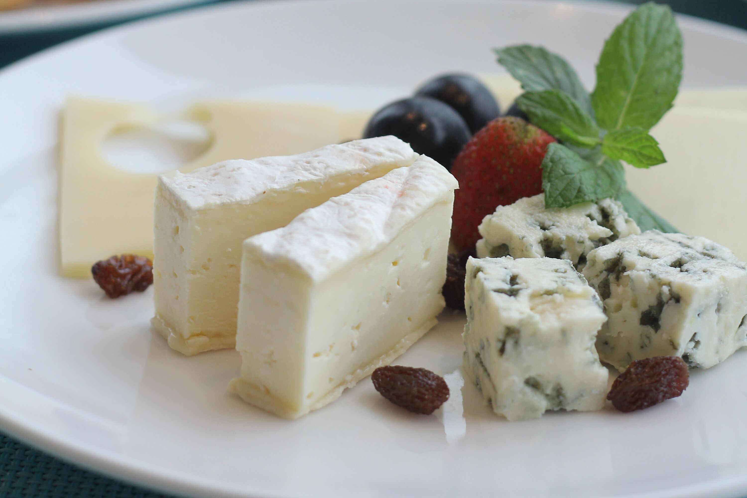 A plate with two types of cheese, a strawberry, and some berries.