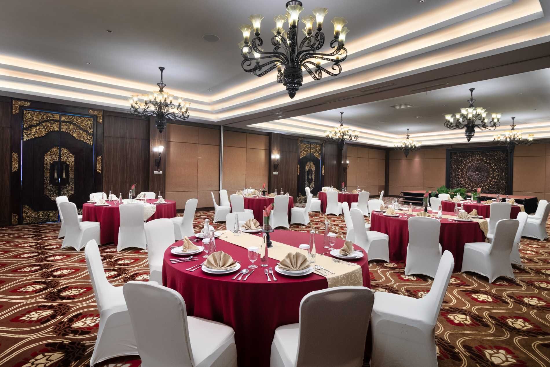 Une salle de banquet avec des tables rondes, des chaises blanches, des lustres et une moquette à motifs.