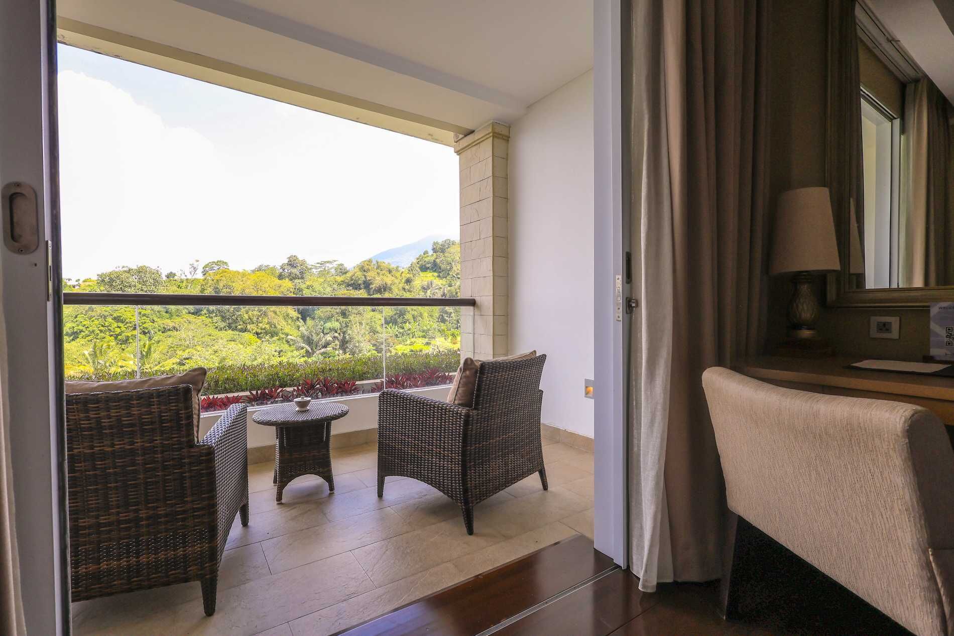 A balcony with wicker furniture, a view of greenery, and a lamp on a table.
