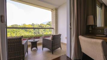 A balcony with wicker furniture, a view of greenery, and a lamp on a table.