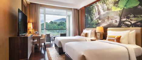 A hotel room with two beds, a desk, a TV, and a large window with a view of greenery.