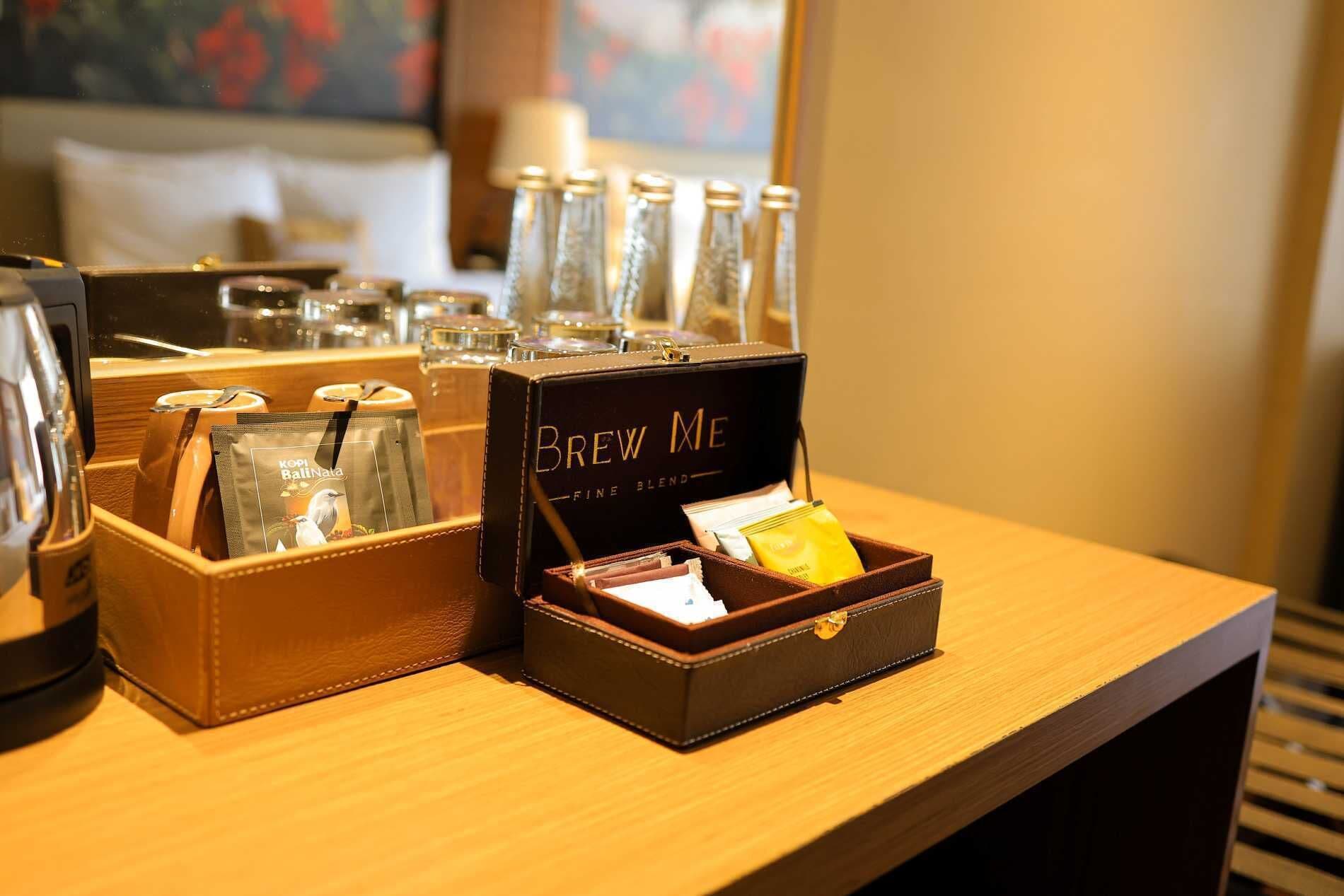 Habitación de hotel con estación de café que incluye una caja de café 'Brew Me', una jarra de vidrio y una cafetera.