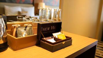 Habitación de hotel con estación de café que incluye una caja de café 'Brew Me', una jarra de vidrio y una cafetera.