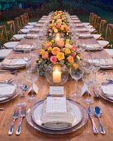 Una larga mesa de comedor dispuesta para un evento formal, con centros de flores, velas y un menú.