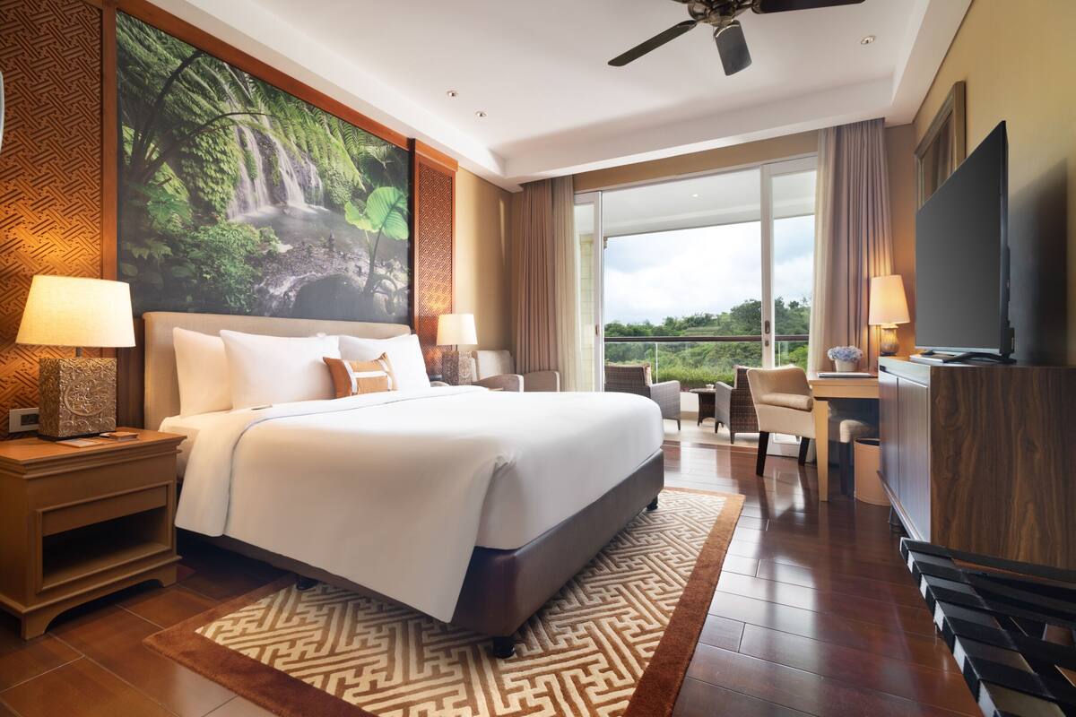 A hotel room with a large bed, a desk, a television, and a view of the outdoors.