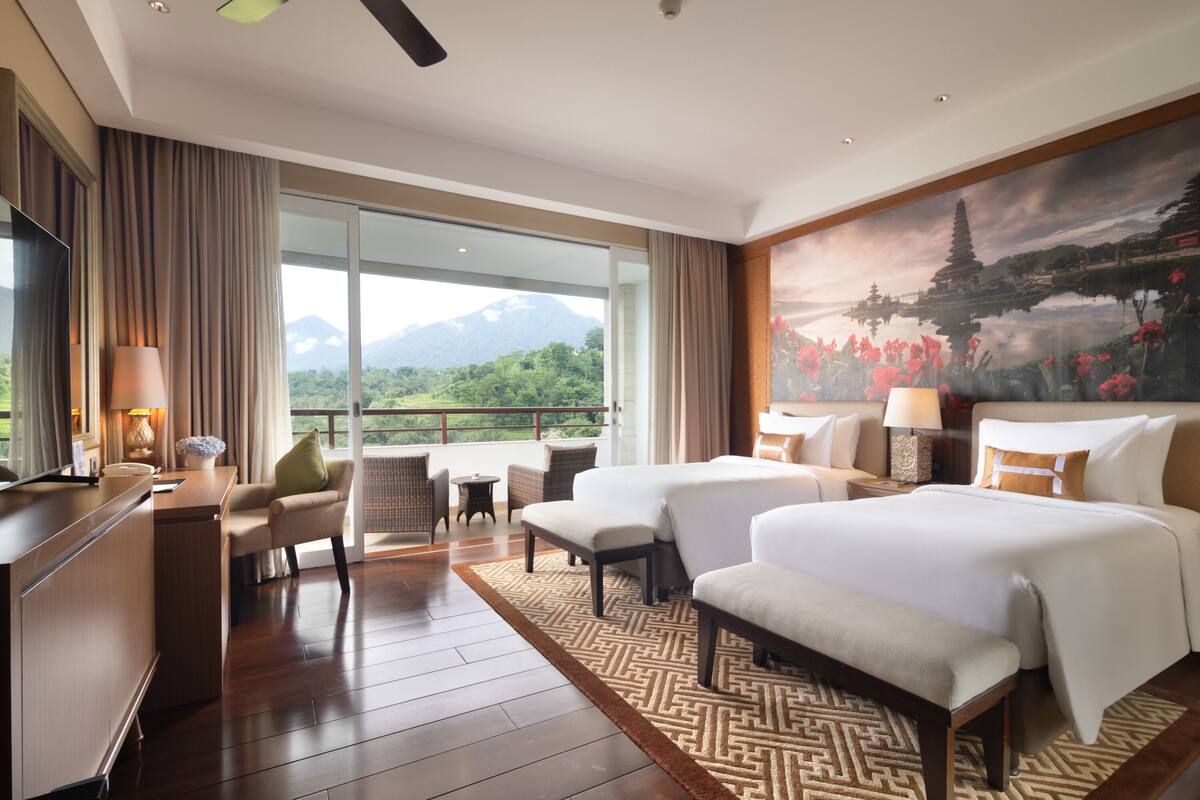 A hotel room with a large bed, a desk, a chair, a small table, and a view of mountains through the window.