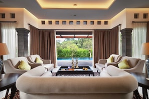 A spacious room with a large window, two sofas, a coffee table, and a view of a pool and greenery. - Homm Saranam Baturiti (Baturiti)