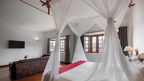 Un dormitorio con cama con dosel, un sofá y un televisor en la pared.