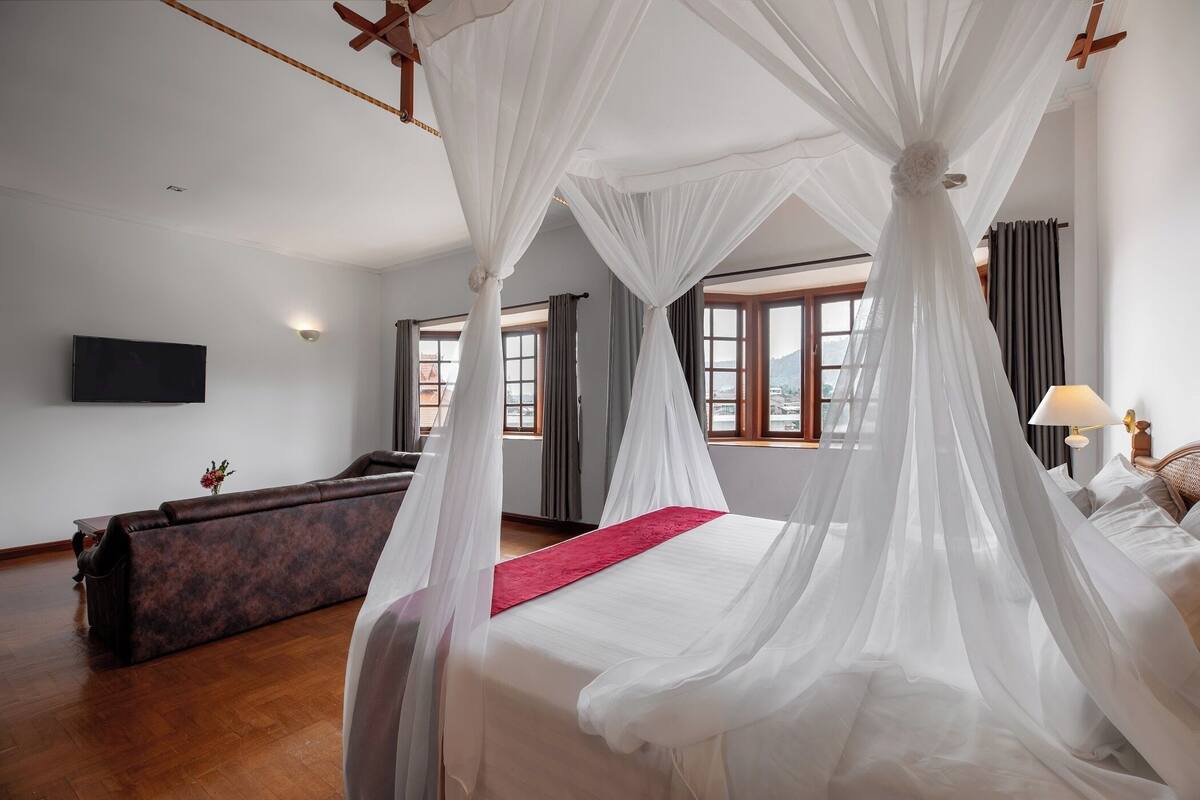 Un dormitorio con cama con dosel, un sofá y un televisor en la pared.