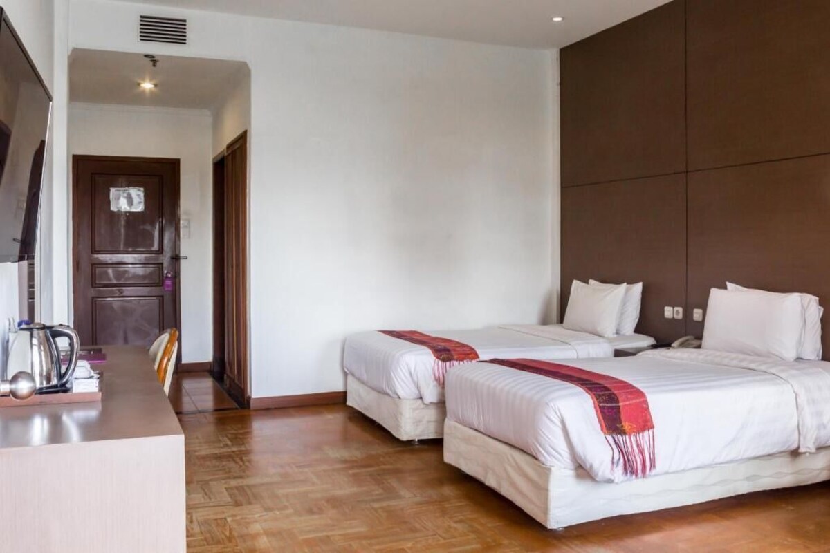 A hotel room with two beds, a desk with a kettle, and a door leading to another room.