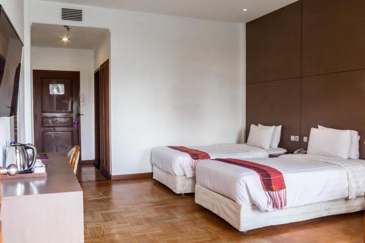 A hotel room with two beds, a desk with a kettle, and a door leading to a bathroom.