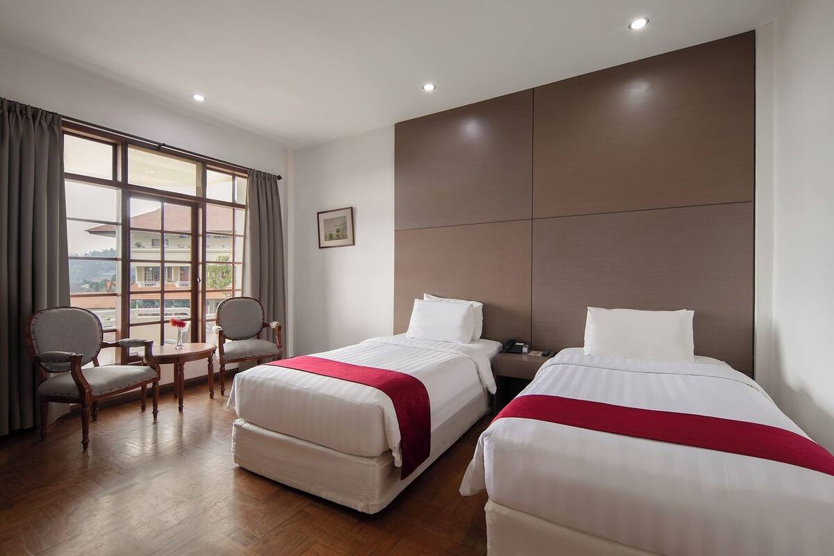 Habitación de hotel con dos camas, suelo de madera, un ventanal grande y vistas a edificios.