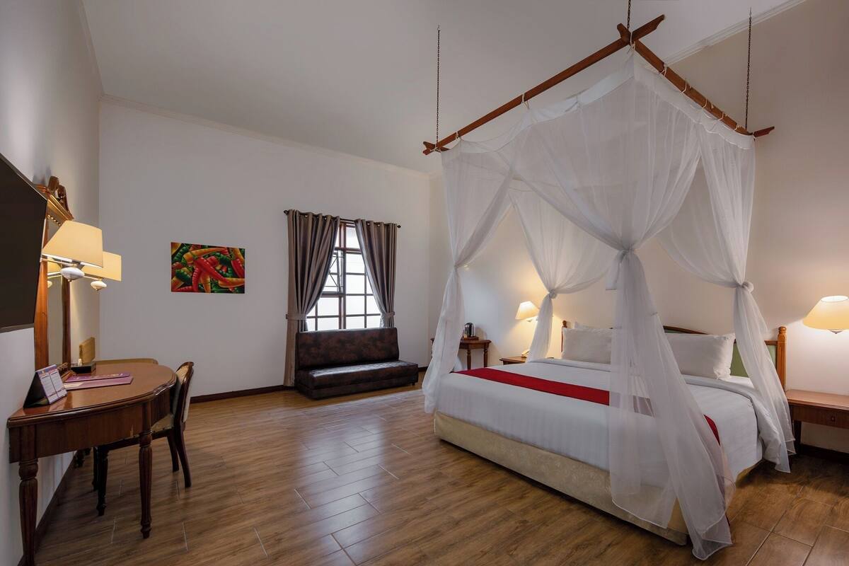 Un dormitorio con una cama con dosel, un escritorio de madera con una silla, un sofá y una ventana con cortinas.