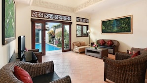 A spacious living area with wicker furniture, a flat-screen TV, and a painting on the wall. - The Batu Belig Hotel & Spa (Keroboken Kelod)
