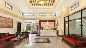 A lobby with a reception desk, wooden sofas, a chandelier, and decorative elements. - The Batu Belig Hotel & Spa (Keroboken Kelod)