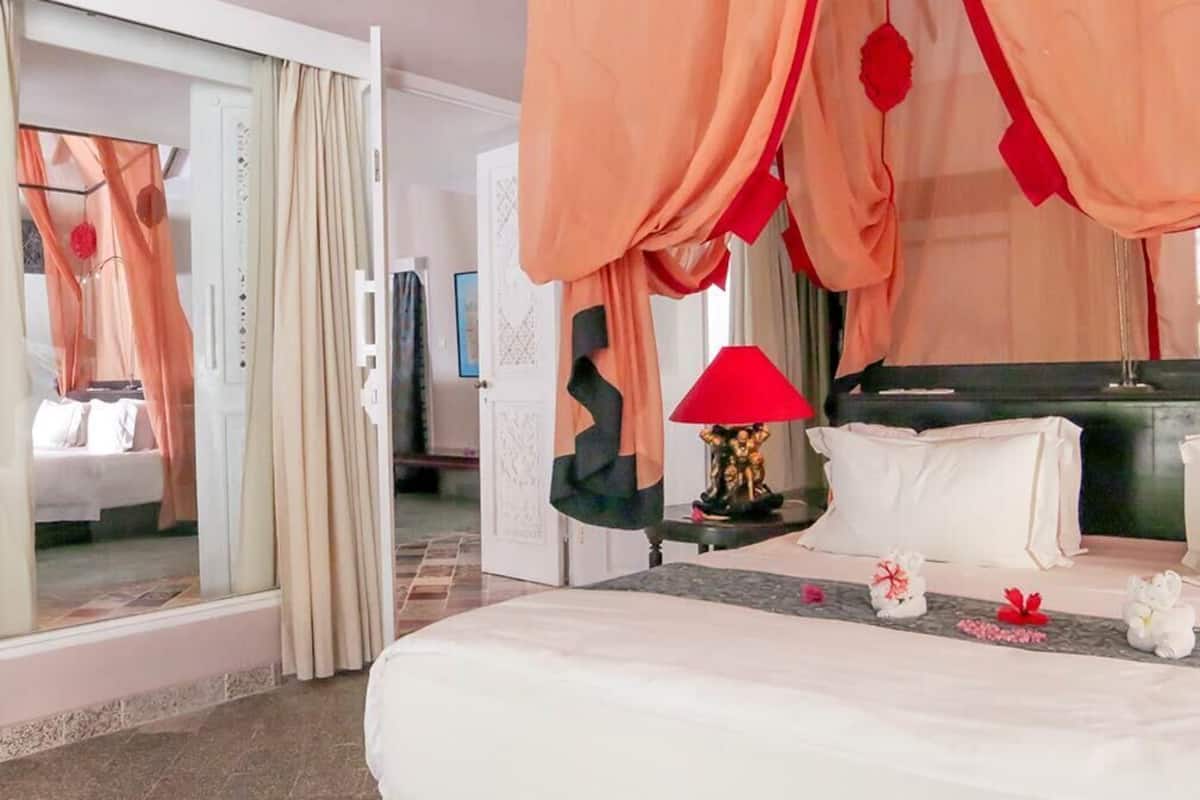 Hotelkamer met een bed, een nachtkastje met lamp en uitzicht op een andere kamer door een glazen deur.