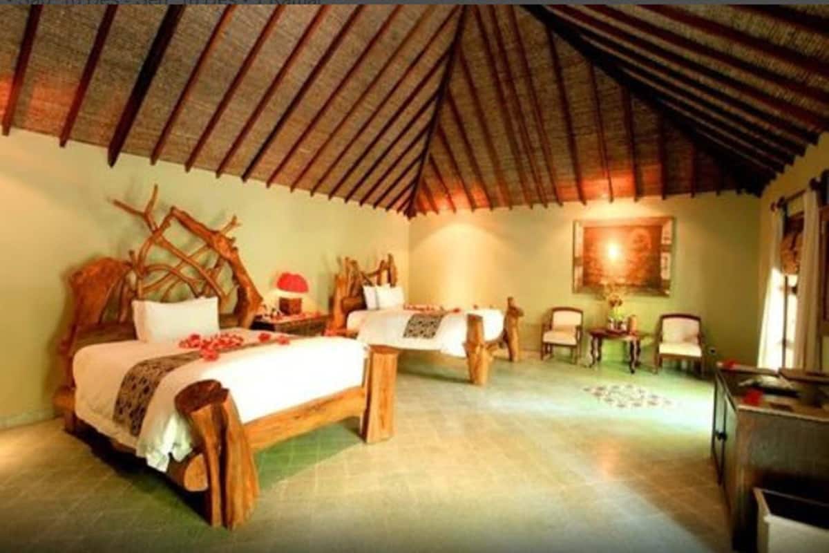 Een kamer met een hoge, schuine plafond, een bed met houten frame, een kleine tafel en stoelen.