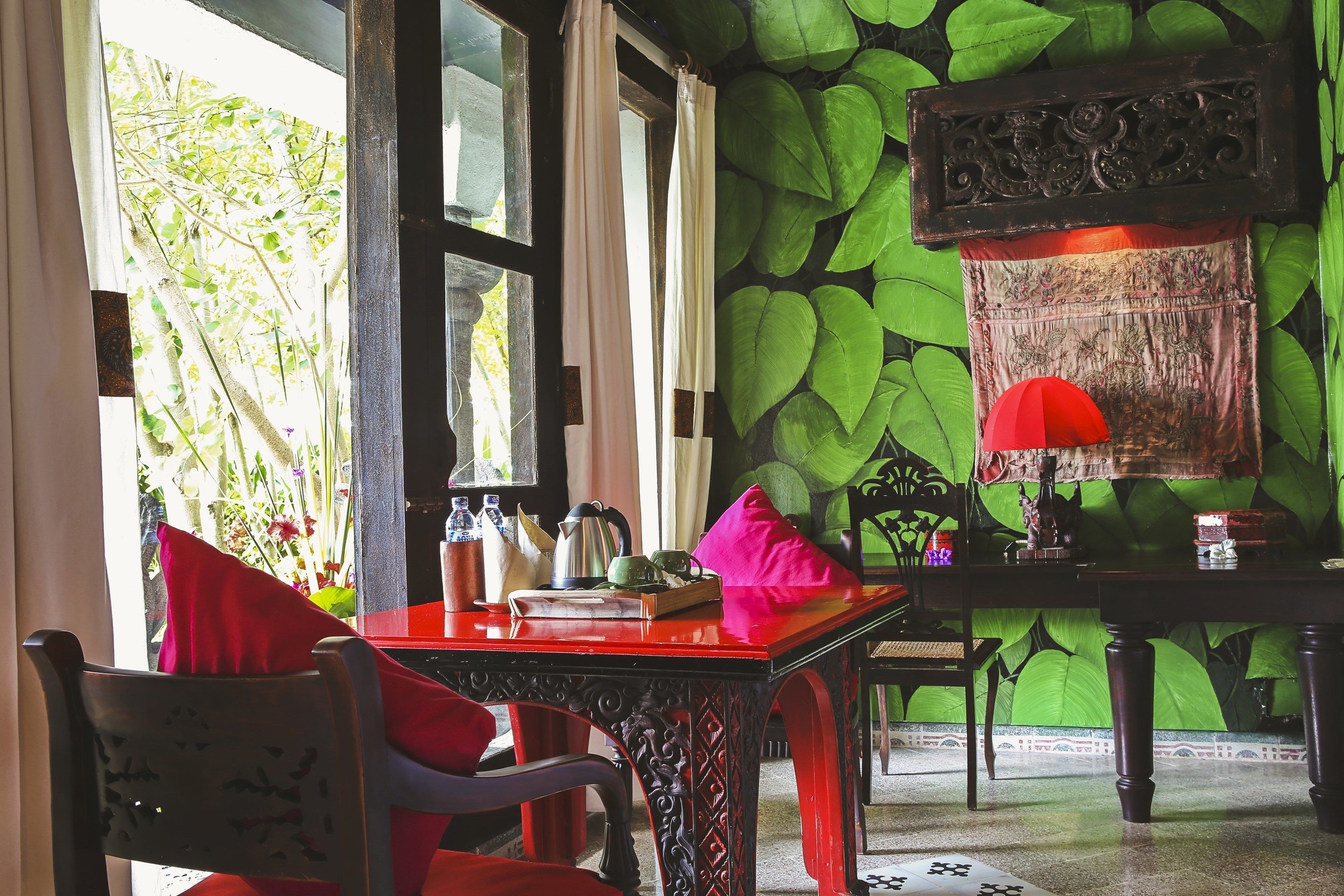 A room with a red table, chairs, and a green leafy wall.