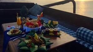 A dining table with a variety of food and drinks, overlooking a body of water and mountains. - Hotel Tugu Lombok (Tanjung)