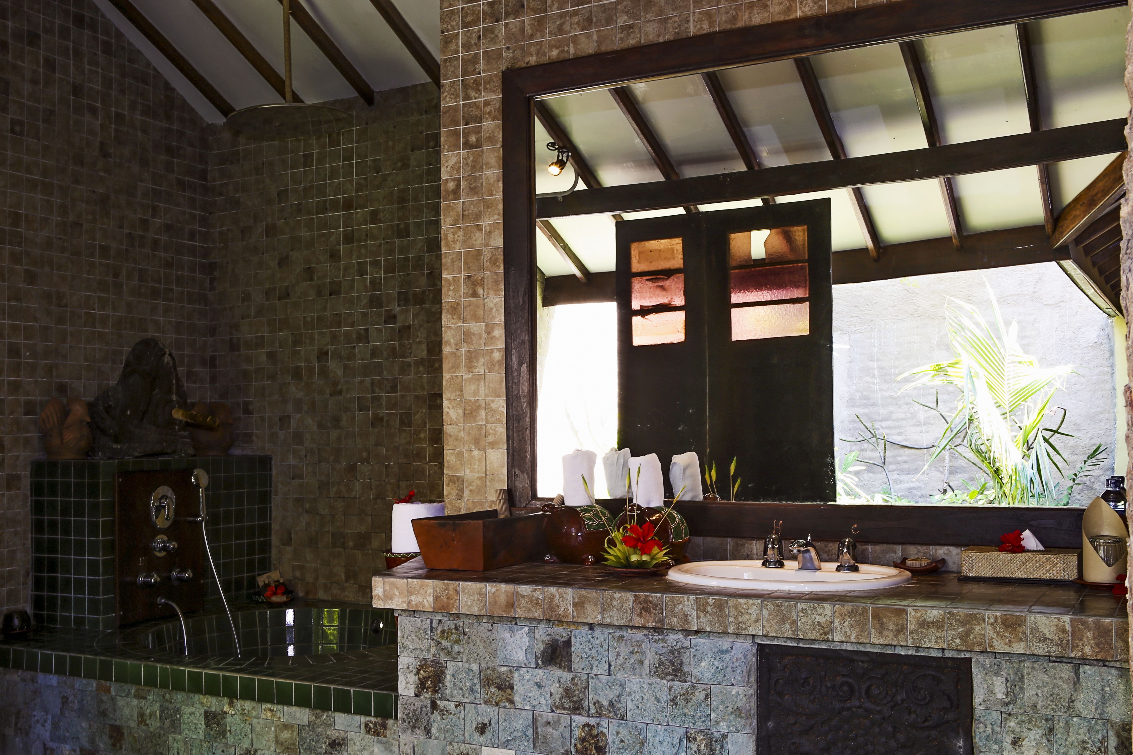 A bathroom with a stone sink, a mirror, and a window with a view of plants.