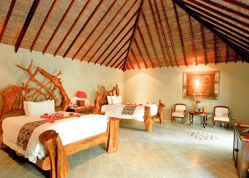 A room with a high thatched roof, wooden furniture, and a bed with a white bedspread and red flowers.
