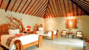 A room with a high thatched roof, wooden furniture, and a bed with a white bedspread and red flowers.