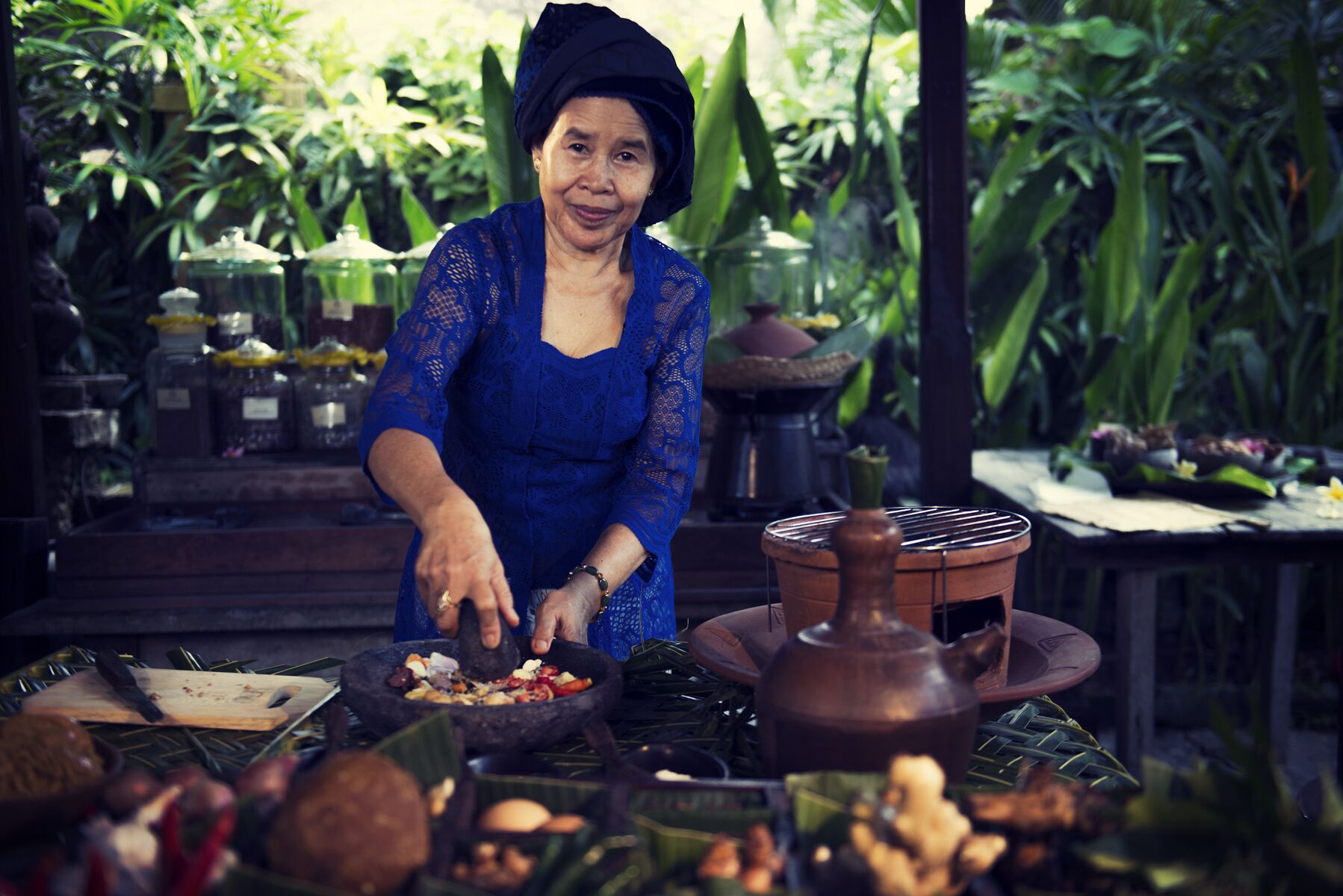 A person preparing food outdoors with a variety of ingredients and cooking utensils visible.
