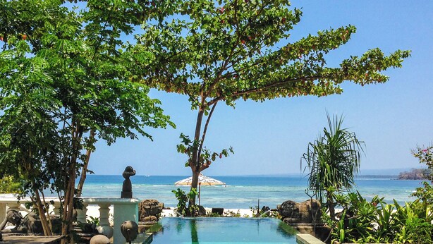 A pool area with a view of the sea, surrounded by trees and stone sculptures. - Hotel Tugu Lombok (Tanjung)