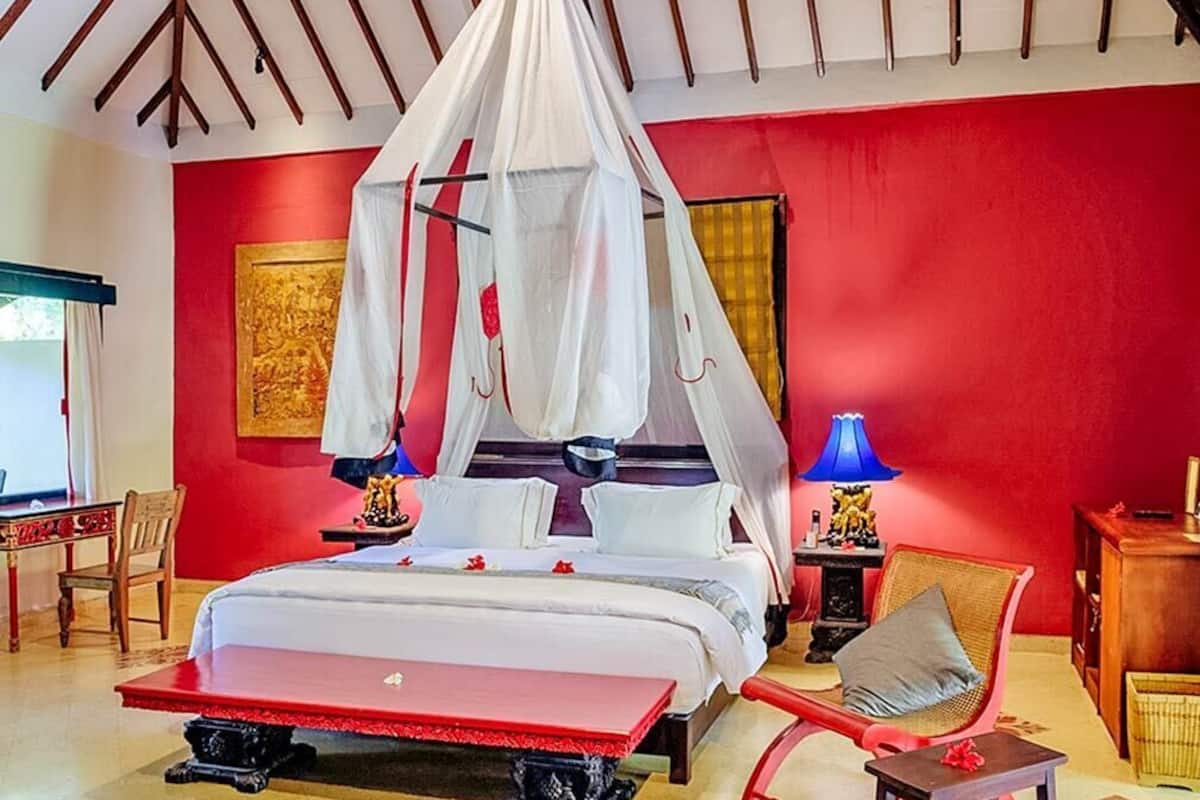 Een slaapkamer met een bed onder een hemelbed, een rode muur en een houten plafond.