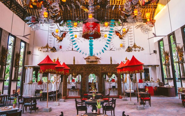 An ornate indoor space with a central decorative structure, tables with chairs, and a patterned floor.