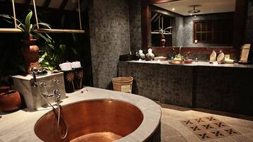 A bathroom with a large copper sink, dark stone walls, and a wooden ceiling.