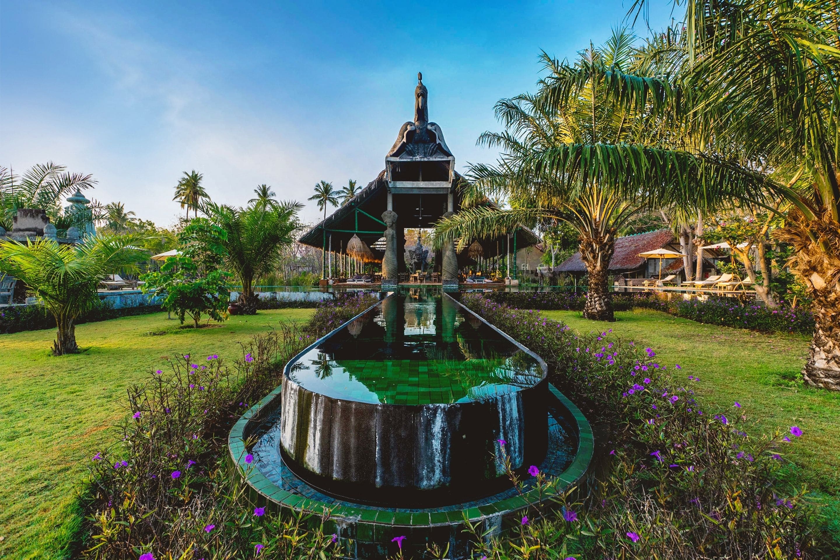 A fountain with a reflective surface surrounded by greenery and a traditional building in the background.