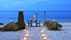 Une scène de plage avec une table et des chaises, entourées de parasols en chaume et de bougies.
