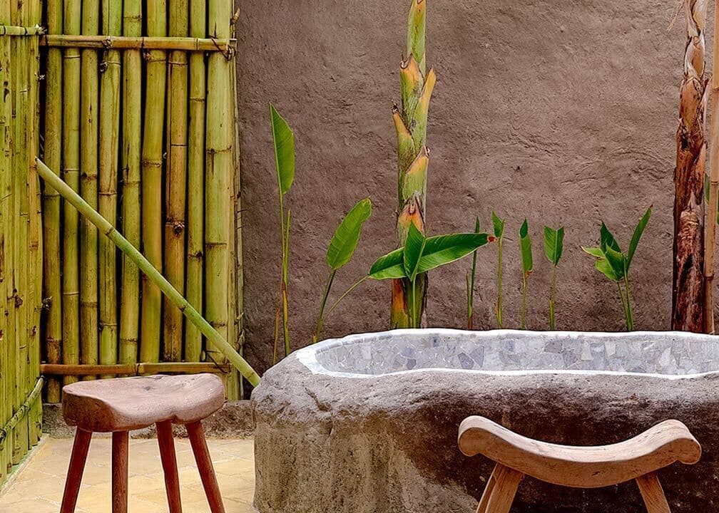 A stone bench, a bamboo fence, and a concrete planter with green plants.