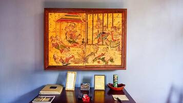 A traditional Chinese painting hanging on a wall above a wooden desk with various items on it.